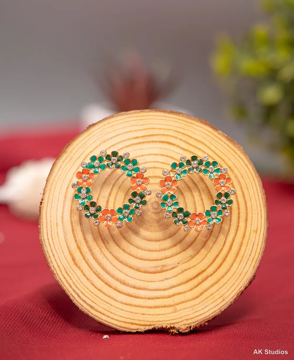 Green and orange enamel floral earrings styled on a natural wood backdrop, color-accurate after editing