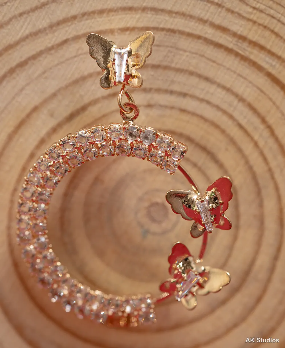 Butterfly-shaped gold and crystal drop earrings photographed at an artistic angle on a wooden surface
