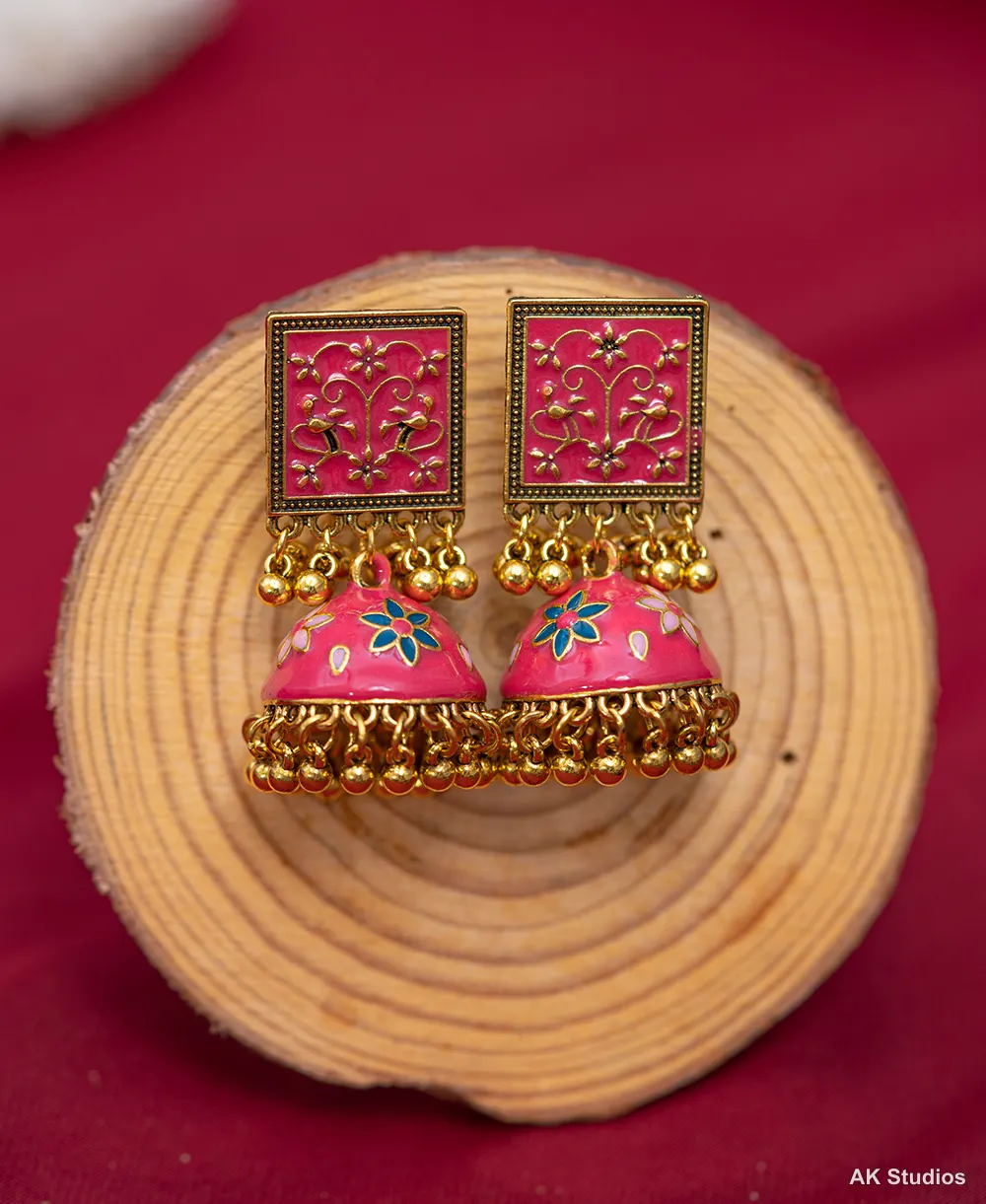 Macro detail of a red and gold jhumka earring showing dangling gold bead charms under soft studio lighting